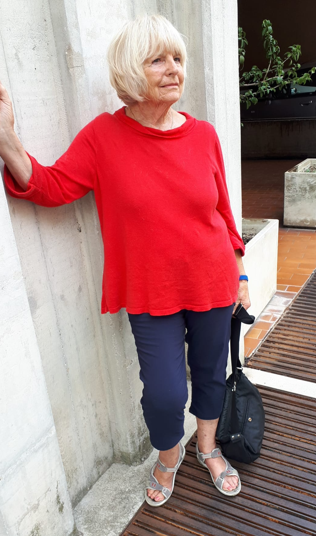 Marianne Igel in einem roten Oberteil und einer dunkelblauen Hose neben einer hellen Steinwand